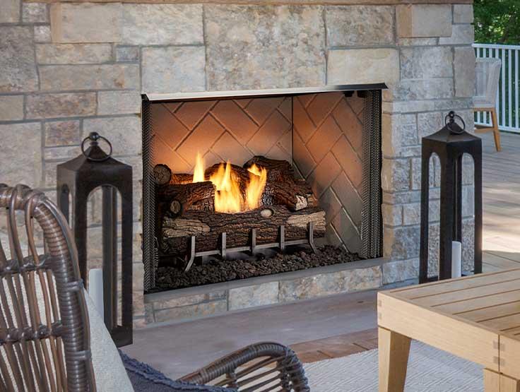 Outdoor vent-free gas fireplace with split logs in three-side covered patio with vaulted wood ceiling.